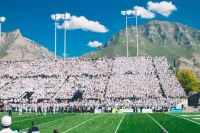 Estádio de futebol americano com bancadas cheias de espectadores e montanhas ao fundo.
