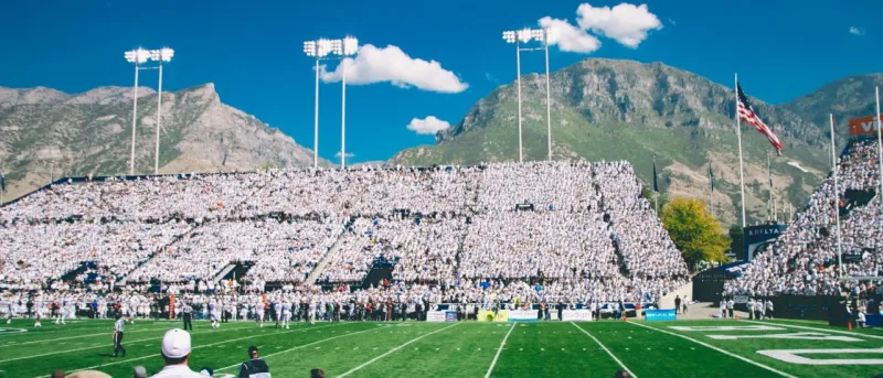 Estádio de futebol americano com bancadas cheias de espectadores e montanhas ao fundo.