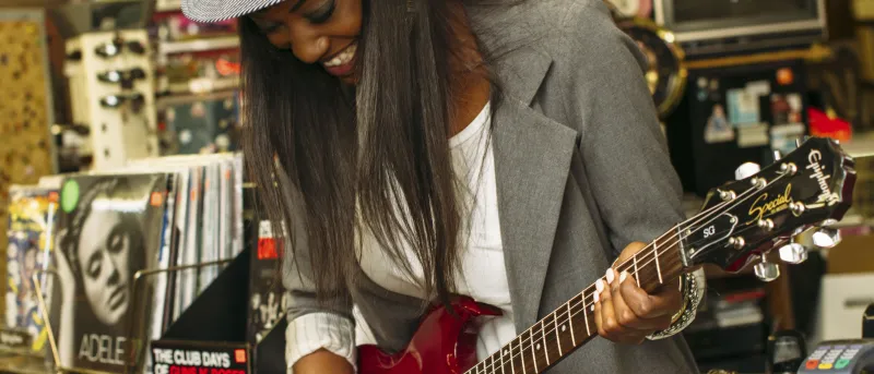 Mulher de chapéu a tocar uma guitarra elétrica vermelha numa loja de música.